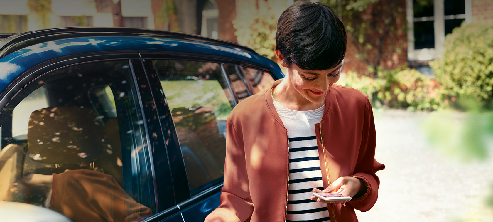 BMW Teleservices, ženska pred BMW-jem gleda svoj pametni telefon